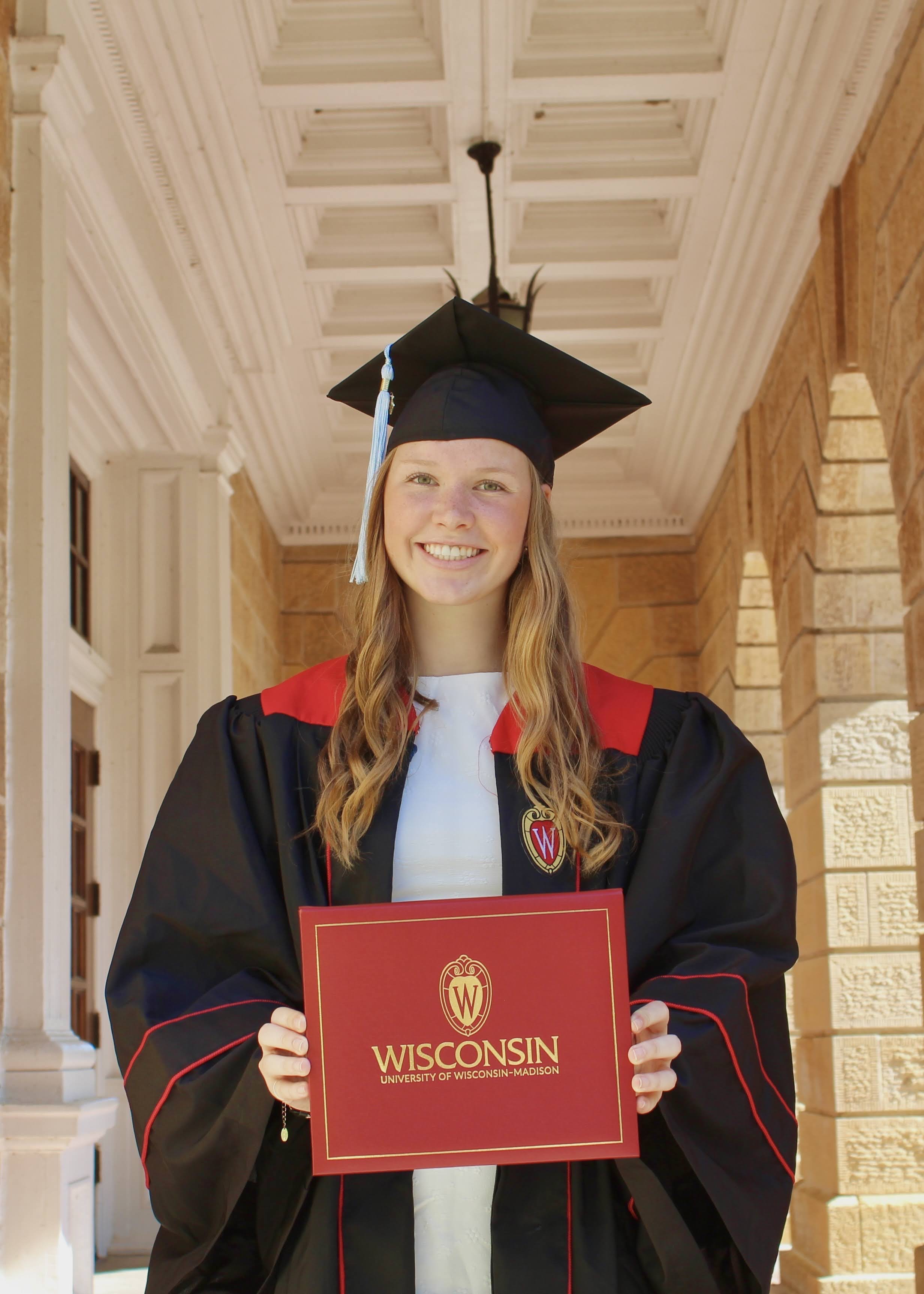 Claire Vandentop wearing graduation cap and gown holding her diploma in front of Bascom Hall.